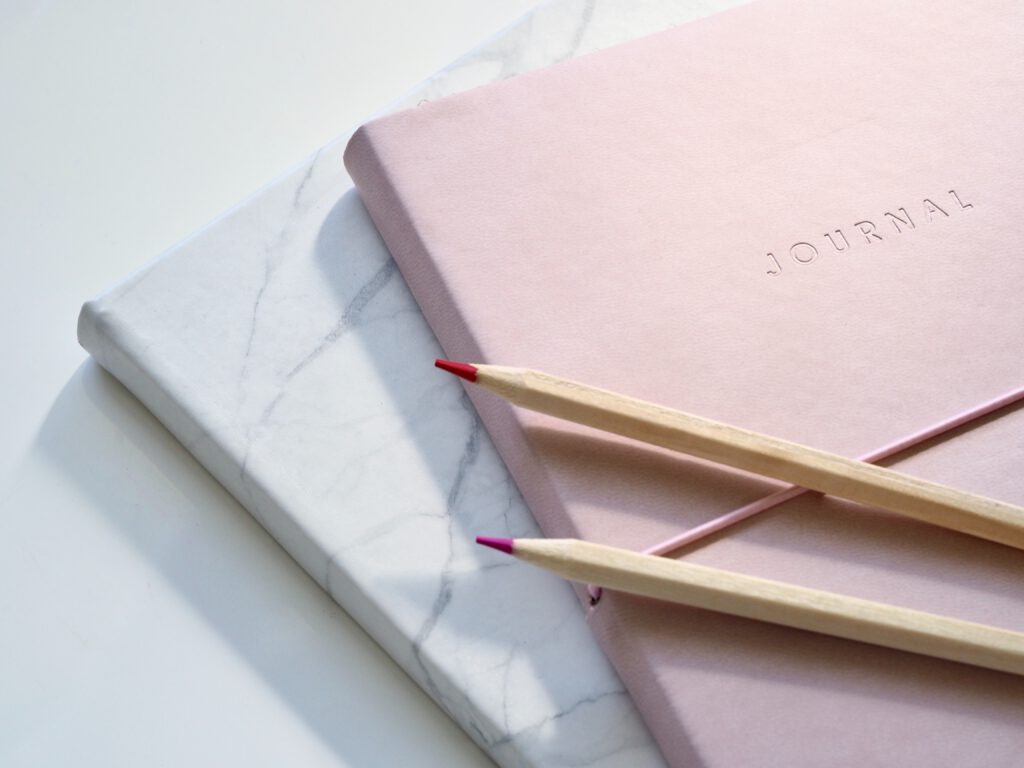 white and pink journal with two pink pencils